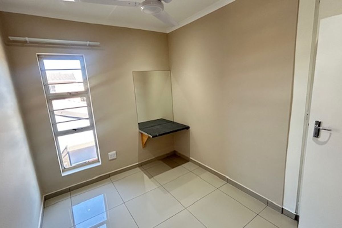 A clean, empty bedroom featuring tiled flooring, a ceiling fan, and a built-in desk with a wall-mounted mirror.