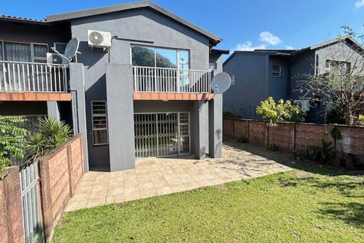 Rear view of the apartment featuring a paved patio area, a balcony with metal railings, and a private garden enclosed by brick boundary walls.