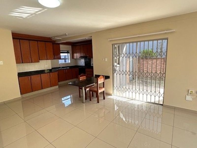 Open-plan living and kitchen area featuring tiled floors, wooden cabinetry, granite countertops, and a sliding door leading to an outdoor space.
