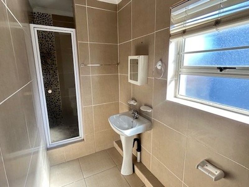 A functional bathroom featuring a pedestal basin, tiled walls and flooring, and a separate shower enclosure with a window for natural light.