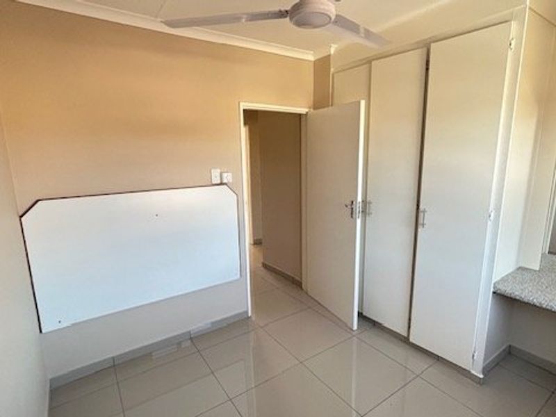 A clean, empty bedroom featuring tiled flooring, built-in cupboards, a ceiling fan, and a built-in vanity area.