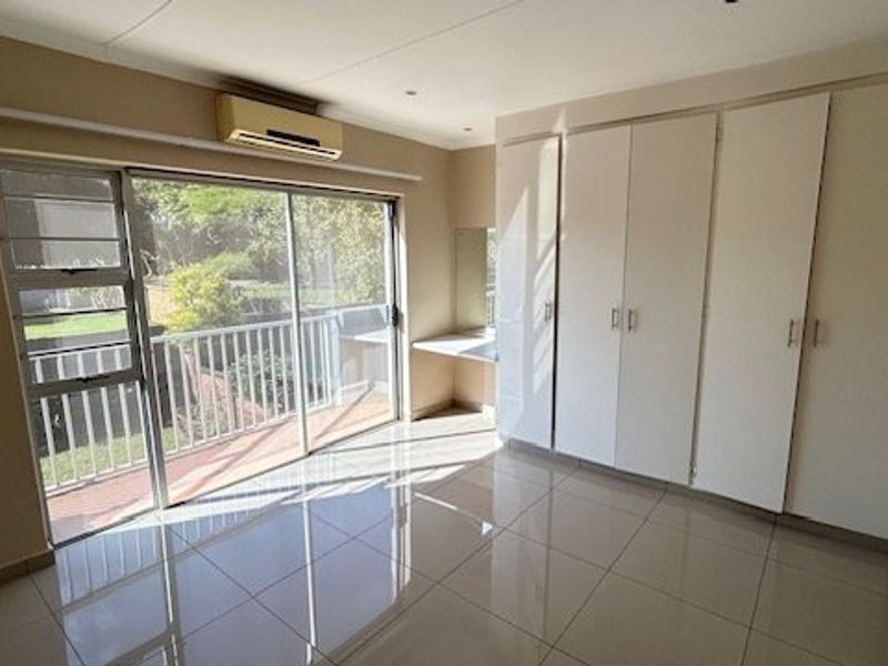 Spacious bedroom featuring large built-in cupboards, a built-in vanity, tiled flooring, and a sliding glass door leading to a balcony with air conditioning.