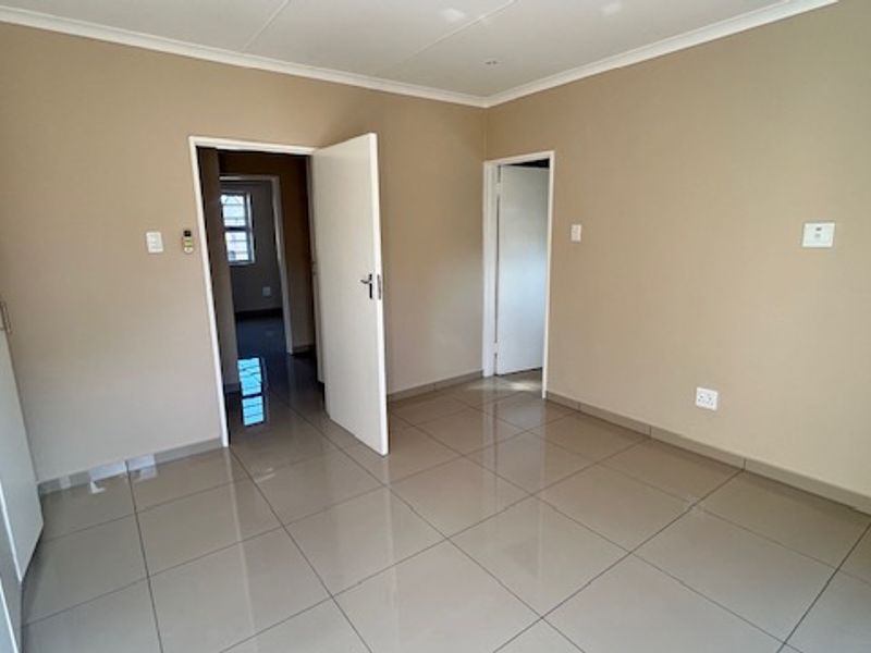 A clean, empty bedroom featuring neutral wall paint, tiled flooring, and built-in cupboards, offering a versatile space ready for personalization.
