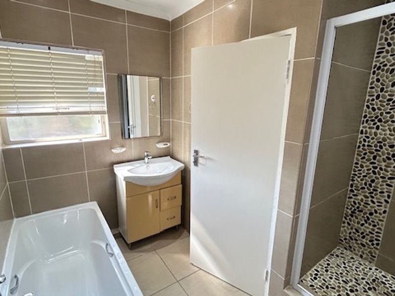 A clean, functional bathroom featuring a bathtub, separate shower enclosure with pebble-style accent tiling, and a vanity cabinet with a basin.