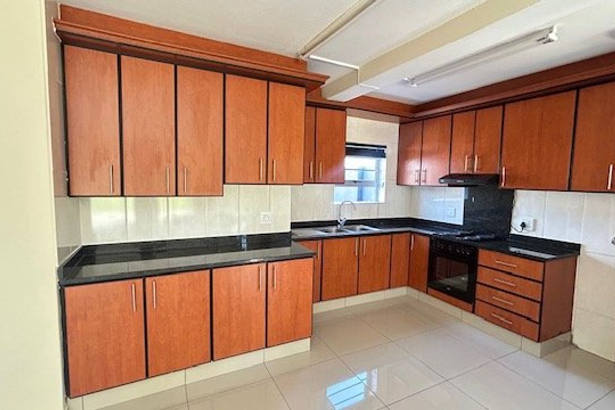 A functional kitchen featuring wooden cabinetry, granite countertops, a built-in oven with hob, and tiled flooring throughout.