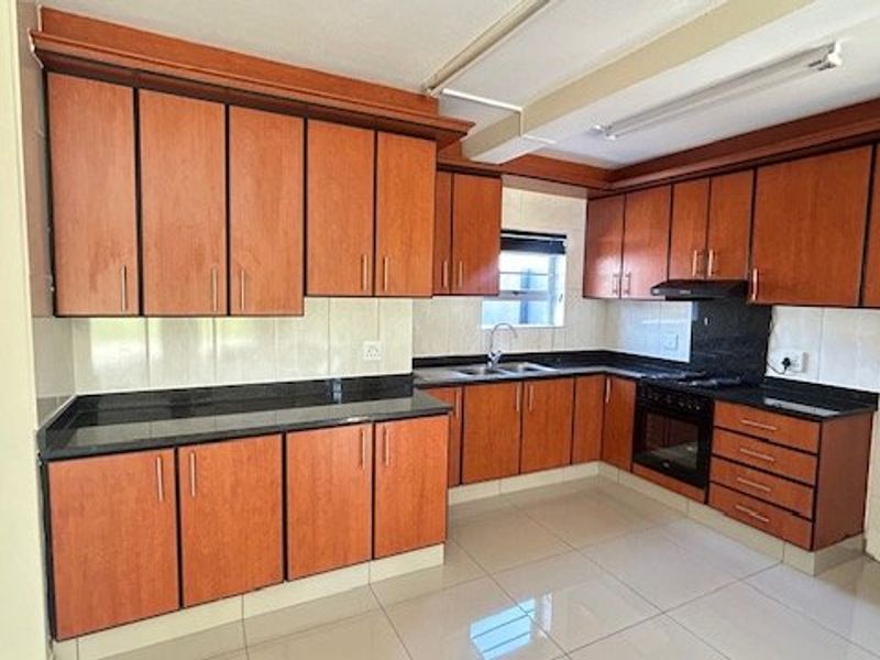 A functional kitchen featuring wooden cabinetry, granite countertops, a built-in oven with hob, and tiled flooring throughout.