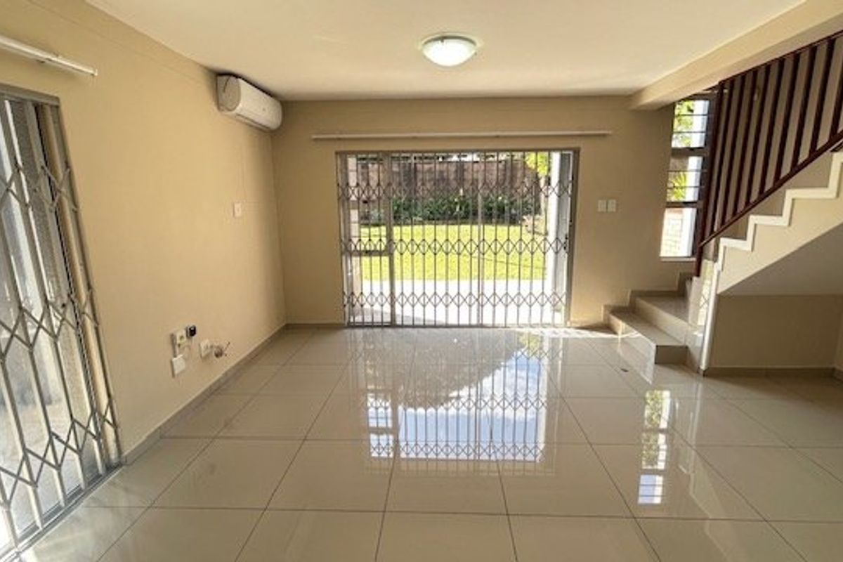 Spacious, light-filled living area featuring neutral tiled flooring, a split-system air conditioner, and direct access to the garden through a secure sliding door.