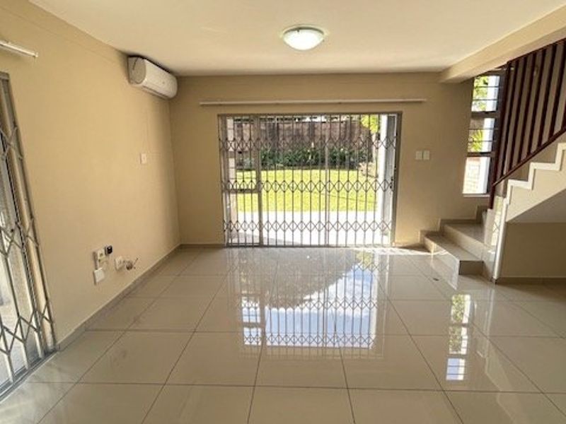 Spacious, light-filled living area featuring neutral tiled flooring, a split-system air conditioner, and direct access to the garden through a secure sliding door.