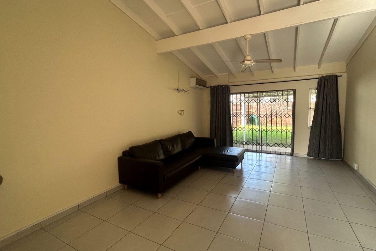 Spacious living room featuring tiled flooring, exposed beam ceiling, ceiling fan, air conditioning, and direct access to the rear garden through a security gate.