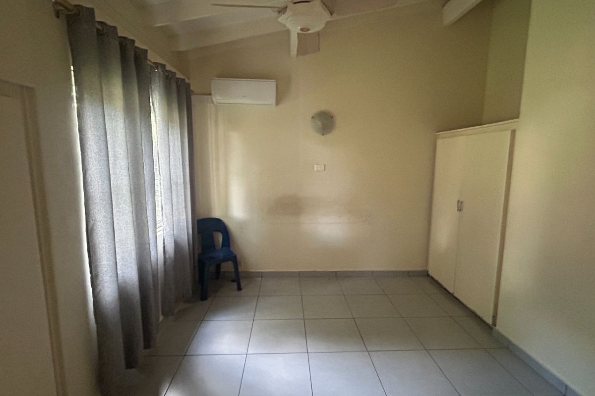 A spacious, neutral bedroom featuring tiled flooring, a built-in wardrobe, and a split-system air conditioner for climate control.