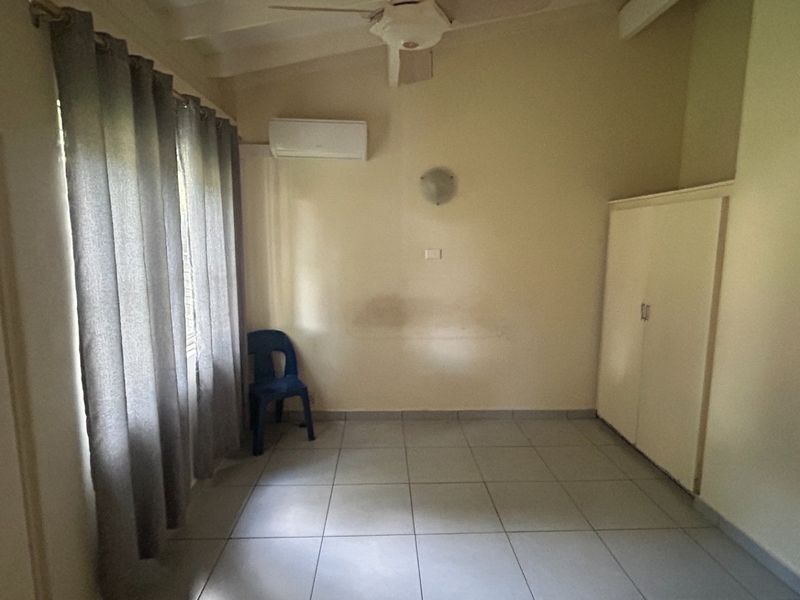 A spacious, neutral bedroom featuring tiled flooring, a built-in wardrobe, and a split-system air conditioner for climate control.