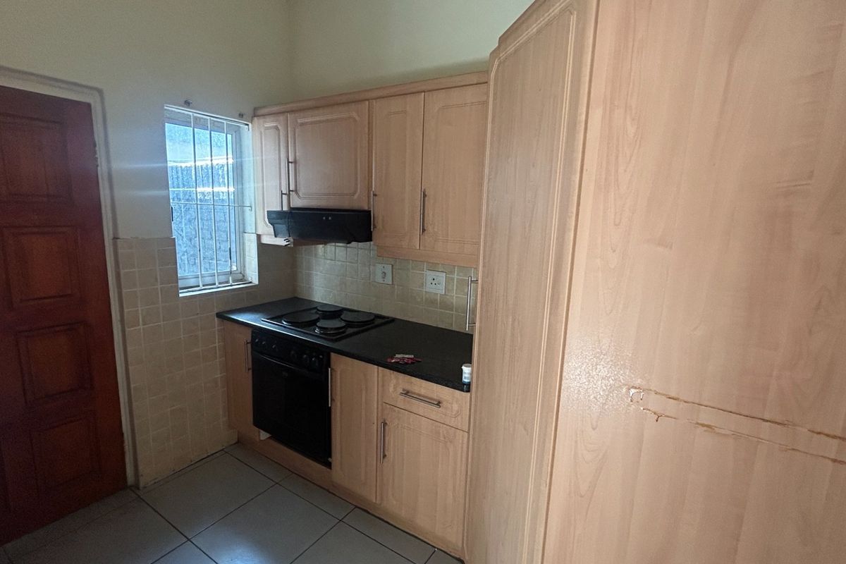 A compact kitchen featuring light wood-finish cabinetry, a built-in oven and hob, tiled backsplash, and tiled flooring.