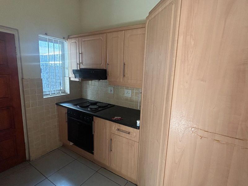 A compact kitchen featuring light wood-finish cabinetry, a built-in oven and hob, tiled backsplash, and tiled flooring.