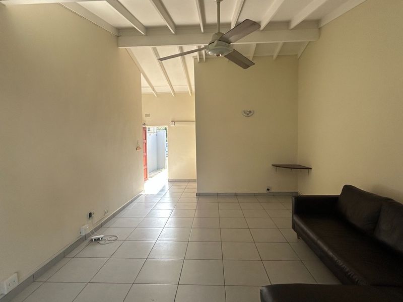 A spacious living area featuring tiled flooring, an exposed beam ceiling with a central fan, and neutral wall finishes.
