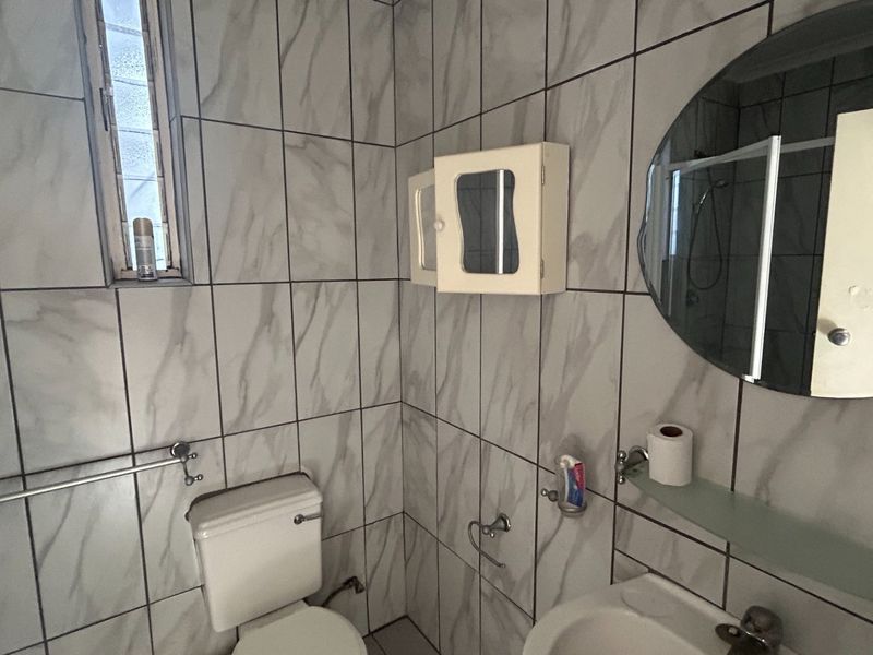 A functional bathroom featuring marble-effect wall tiles, a wall-mounted medicine cabinet, a circular mirror, and a standard toilet and basin setup.