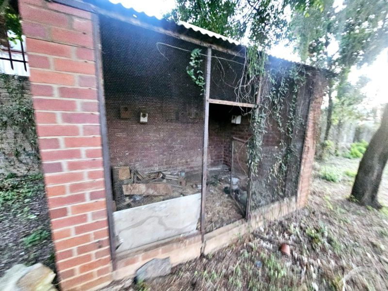 A dilapidated brick and wire mesh utility structure located on the residential land, showing significant signs of weathering and neglect.