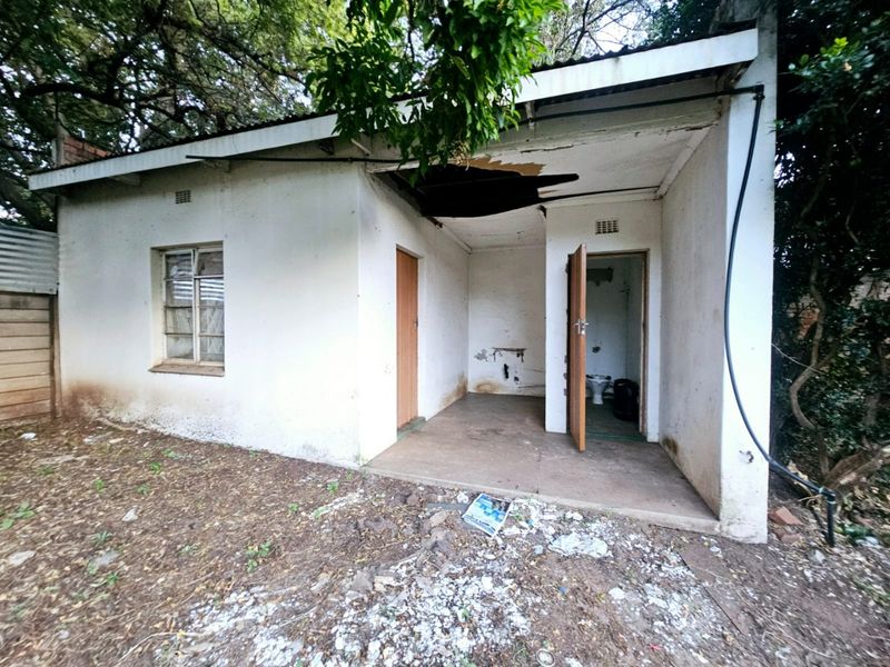 Exterior view of a small outbuilding showing significant structural damage to the roof and exterior walls, requiring major repairs or renovation.