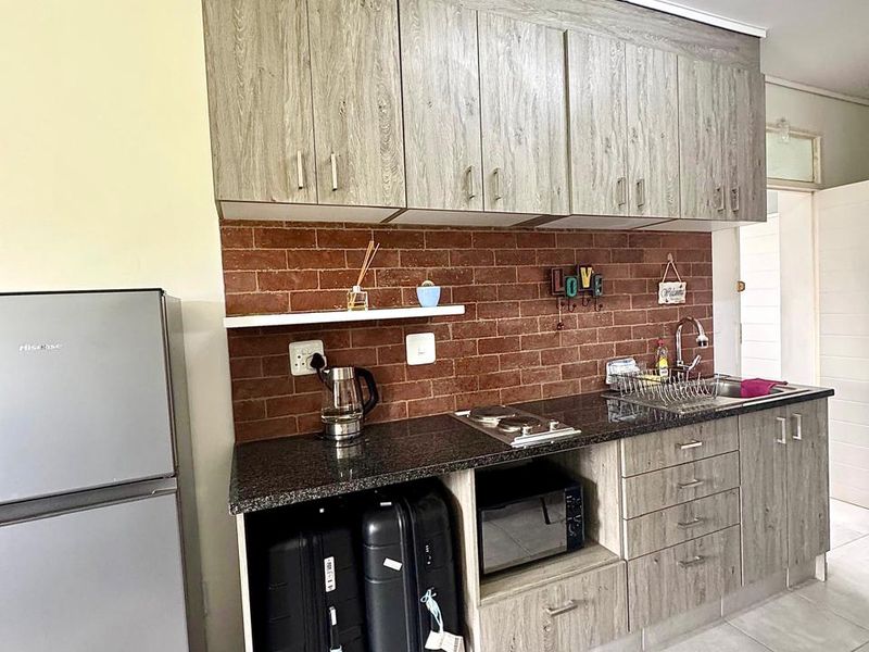 Compact kitchen featuring wood-look cabinetry, granite countertops, a brick-style backsplash, and integrated appliances, offering a functional layout for an apartment.