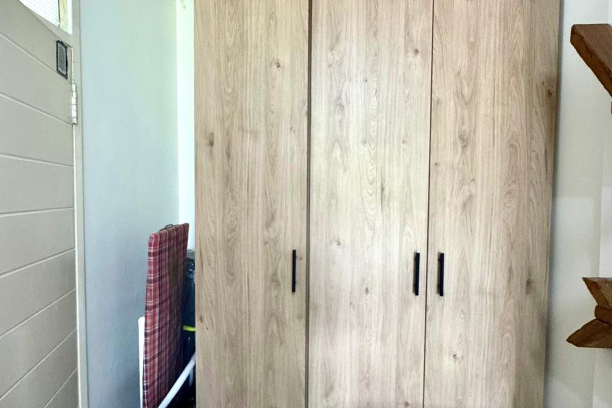 A bedroom featuring a modern, light wood-grain built-in wardrobe with sleek black handles, providing ample storage space.