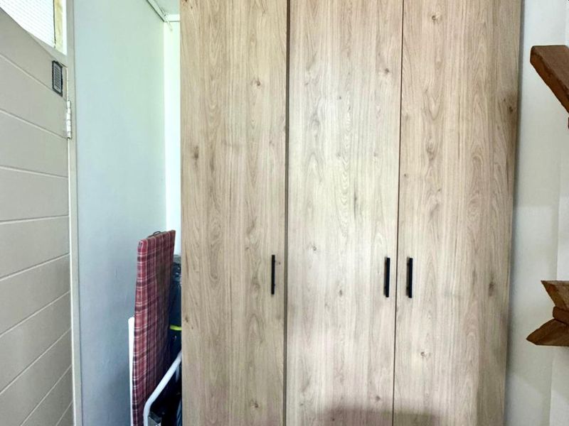 A bedroom featuring a modern, light wood-grain built-in wardrobe with sleek black handles, providing ample storage space.