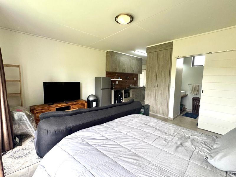 Open-plan studio apartment featuring a kitchenette with built-in cabinetry, tiled flooring, and an adjoining bathroom with a sliding door entrance.