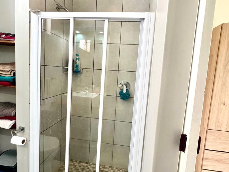 A functional bathroom shower featuring a sliding glass door, tiled walls, and a mosaic floor finish with adjacent built-in shelving.
