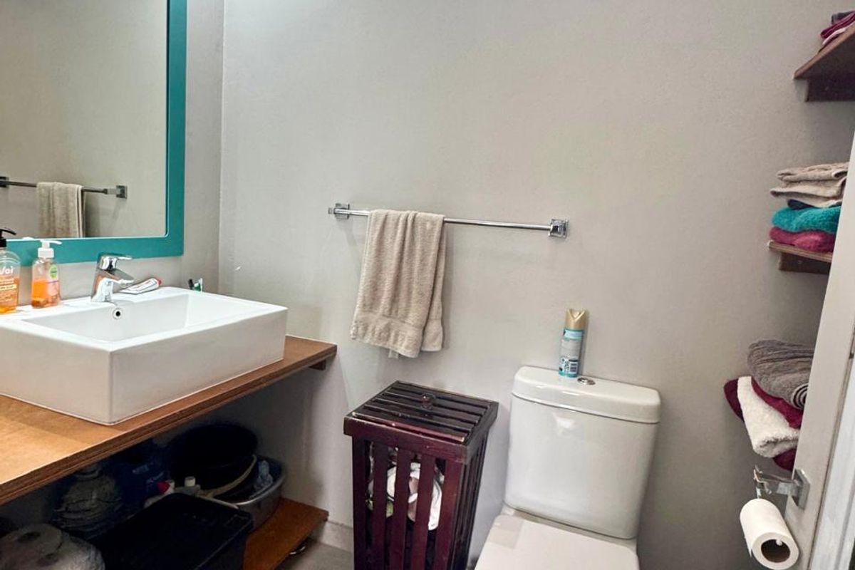 A compact bathroom featuring a vessel sink on a wooden vanity, a standard toilet, and a high-level window for natural light.