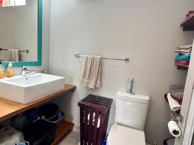 A compact bathroom featuring a vessel sink on a wooden vanity, a standard toilet, and a high-level window for natural light.