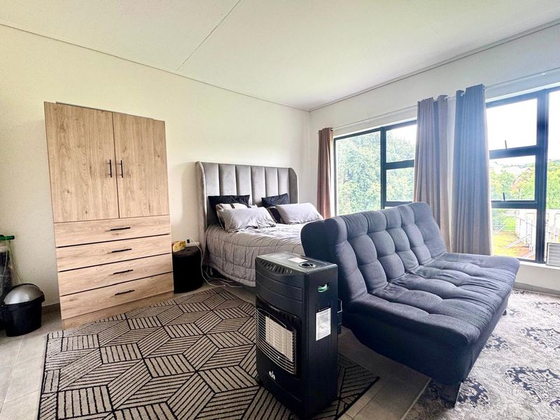 A well-lit bedroom featuring large windows, neutral walls, and tiled flooring, providing a comfortable and functional living space.
