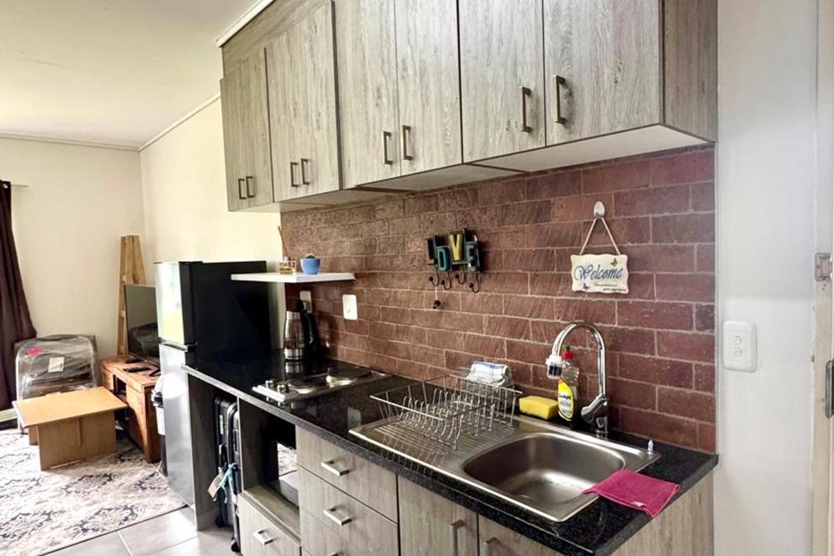 Compact kitchen featuring wood-look laminate cabinetry, granite countertops, a stainless steel sink, and a decorative brick-style backsplash.