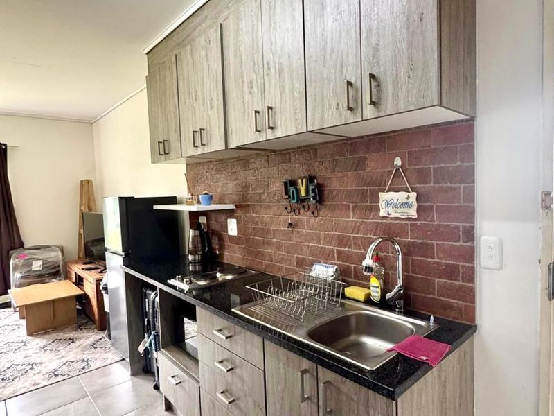 Compact kitchen featuring wood-look laminate cabinetry, granite countertops, a stainless steel sink, and a decorative brick-style backsplash.