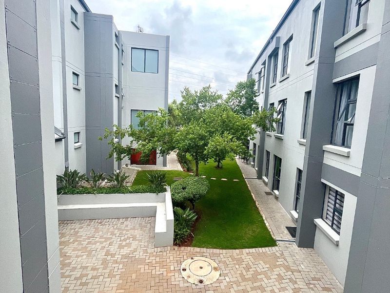 A view of the apartment complex courtyard featuring paved walkways, landscaped garden areas, and modern multi-story building facades.
