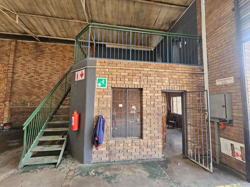Industrial utility space featuring a mezzanine level with metal staircase, exposed brick walls, security gate, and essential safety infrastructure.