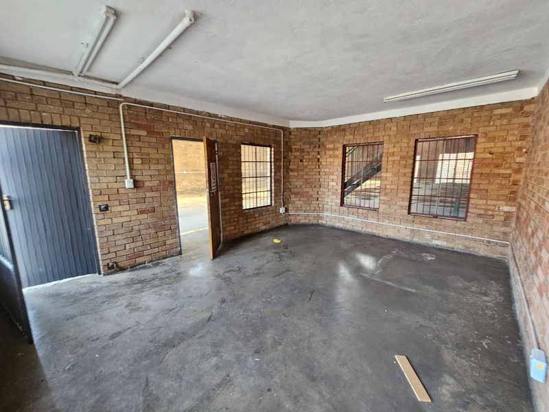 An empty industrial utility space featuring exposed brick walls, concrete flooring, and functional fluorescent lighting, suitable for storage or workshop use.