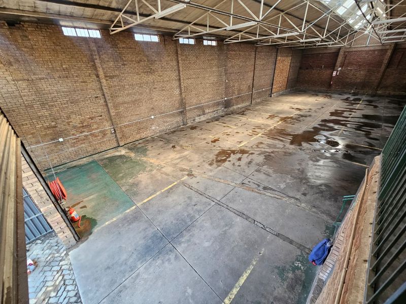Spacious industrial warehouse unit featuring exposed brick walls, high truss ceilings with skylights, and durable concrete flooring suitable for various commercial or storage uses.
