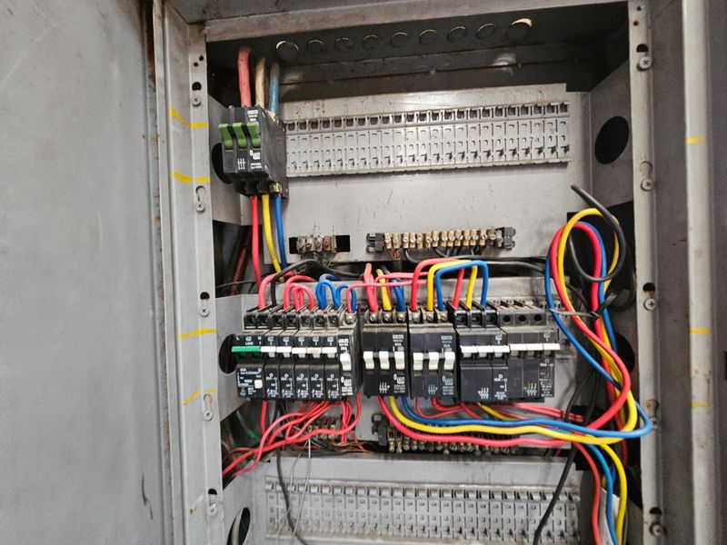 Industrial electrical distribution board with exposed wiring and circuit breakers, showing signs of age and wear.