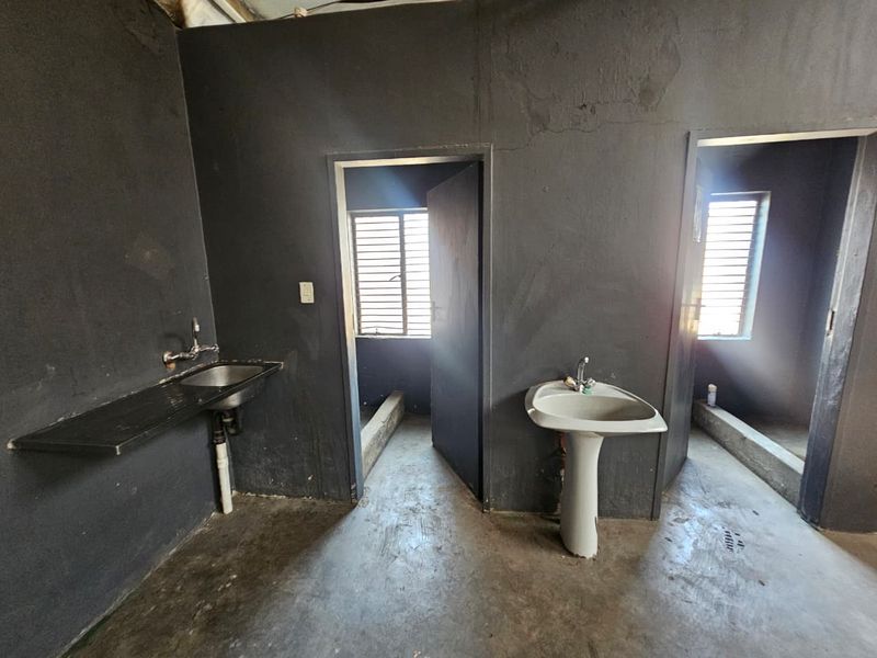 Utility space featuring a wall-mounted sink, pedestal basin, and louvered windows, with dark painted walls and concrete flooring.