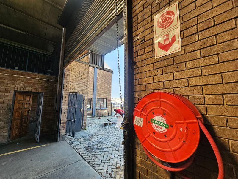 Industrial garage space featuring a roller shutter door, fire safety equipment, and exposed brick walls, with access to an external paved courtyard area.
