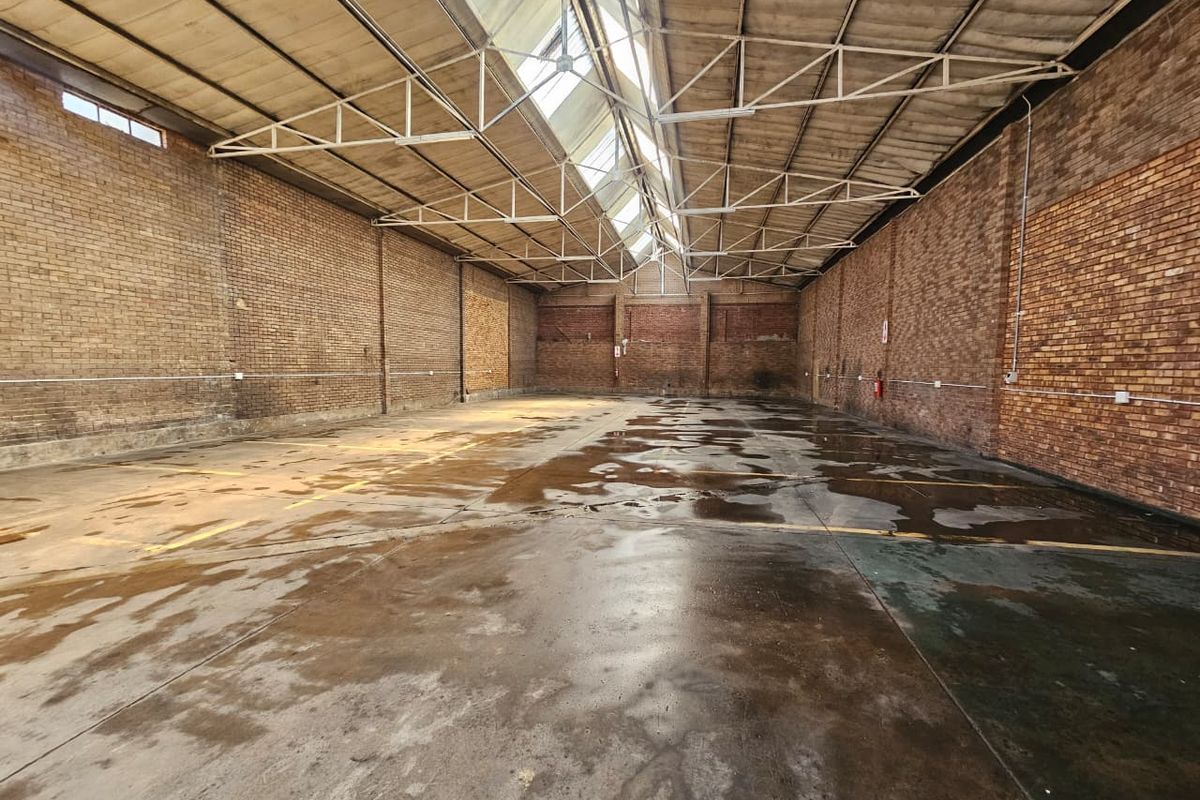 Spacious industrial warehouse unit featuring exposed brick walls, high truss ceilings with integrated skylights, and durable concrete flooring.