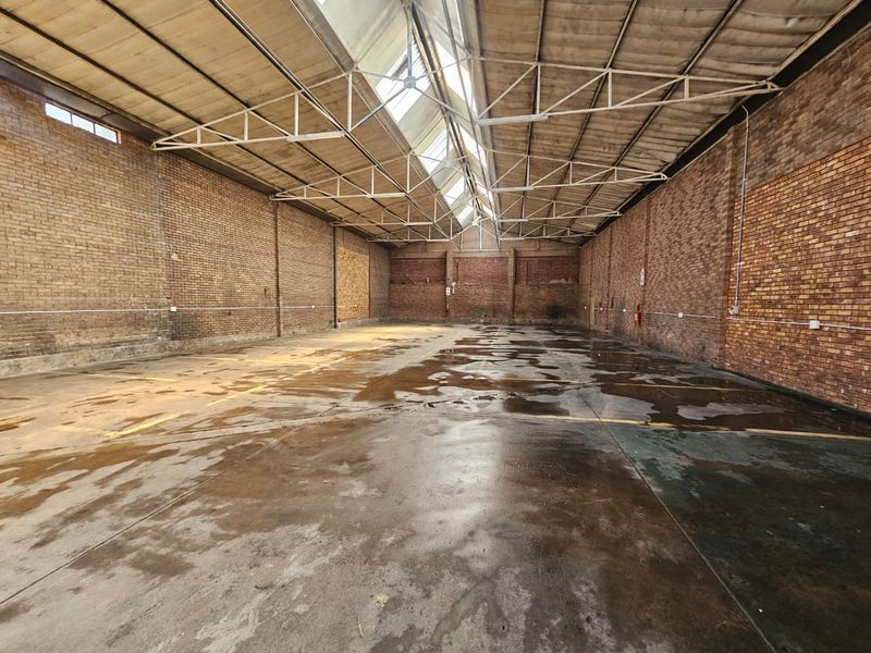 Spacious industrial warehouse unit featuring exposed brick walls, high truss ceilings with integrated skylights, and durable concrete flooring.