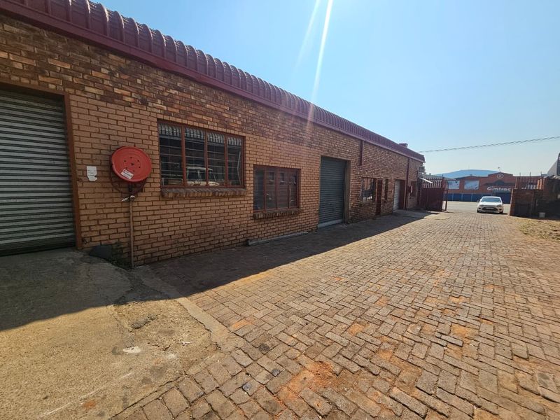 Industrial property exterior featuring a brick facade, multiple roller shutter doors, and a paved driveway area.