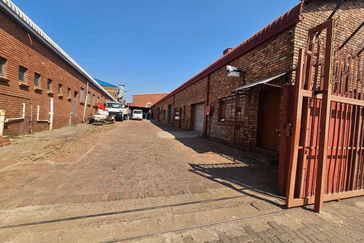 Industrial exterior view featuring brick warehouse buildings, a paved driveway, and secure gated access.