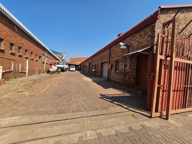 Industrial exterior view featuring brick warehouse buildings, a paved driveway, and secure gated access.