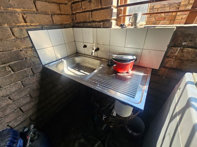 A functional scullery area featuring a stainless steel sink, tiled splashback, and exposed brick walls, suitable for utility or prep work.