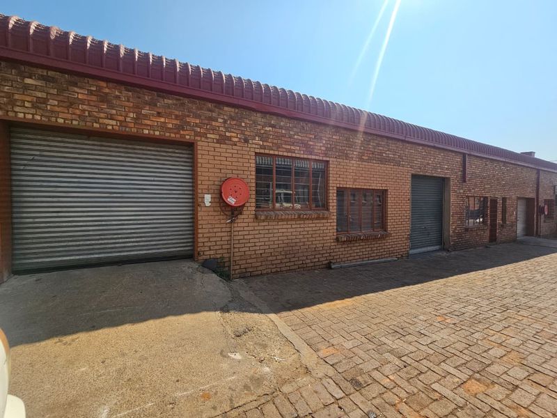 Industrial property exterior featuring a brick facade, multiple roller shutter doors, and a paved driveway area.