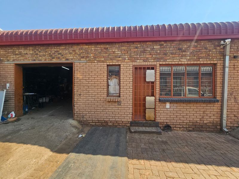 Industrial property exterior featuring a face brick facade, large roller shutter access, security gate, and paved driveway area.