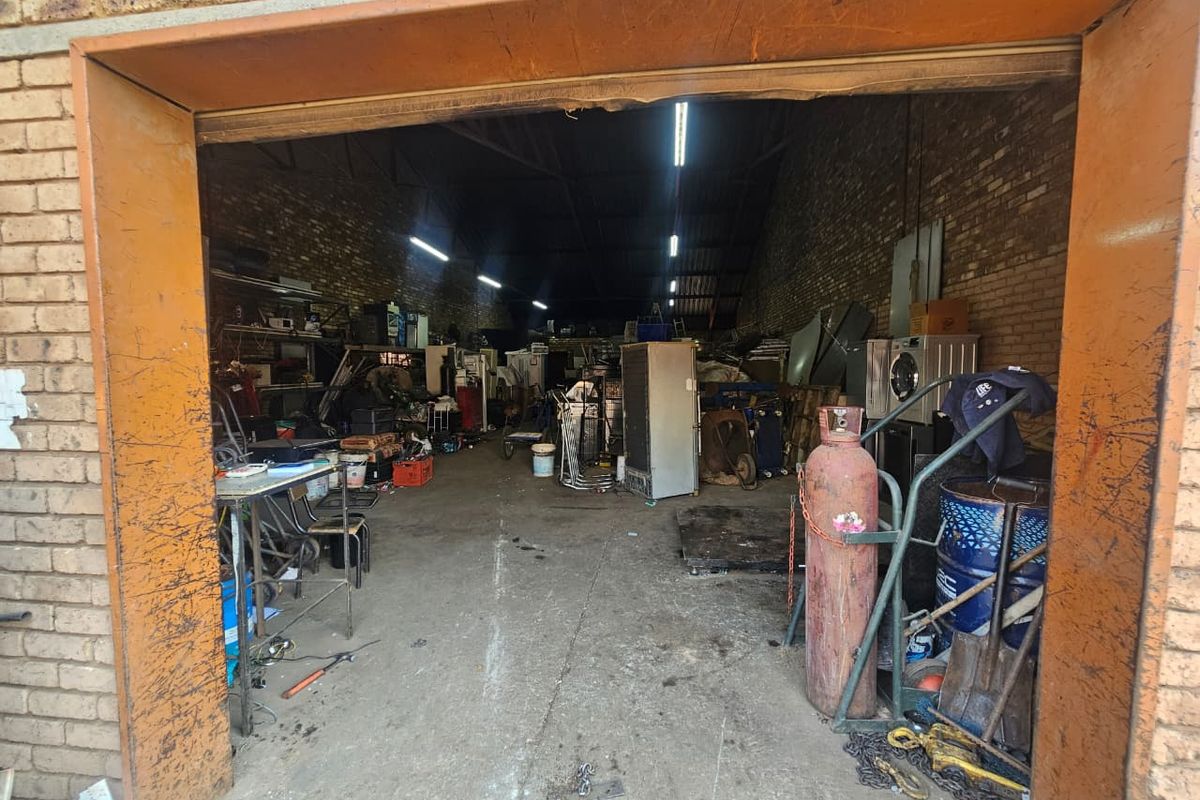 A spacious industrial garage or workshop area featuring exposed brick walls, concrete flooring, and overhead fluorescent lighting, suitable for storage or light industrial use.