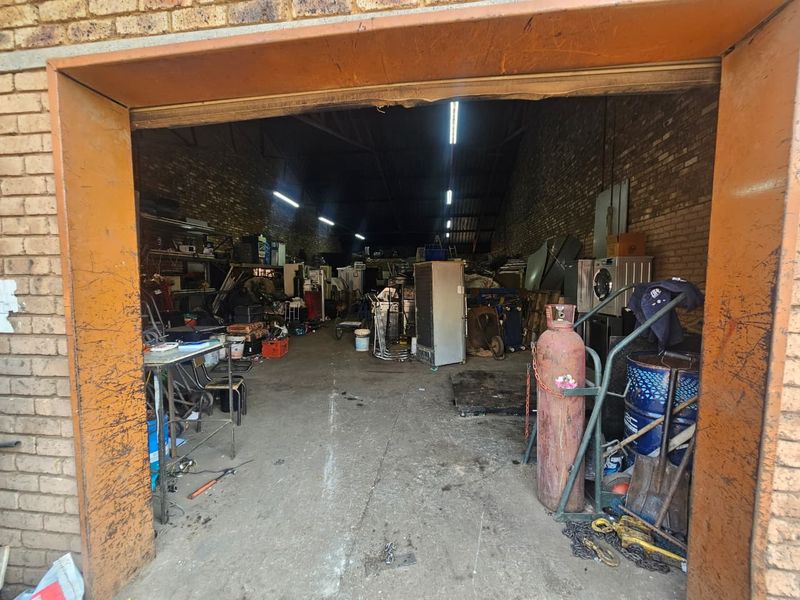 A spacious industrial garage or workshop area featuring exposed brick walls, concrete flooring, and overhead fluorescent lighting, suitable for storage or light industrial use.