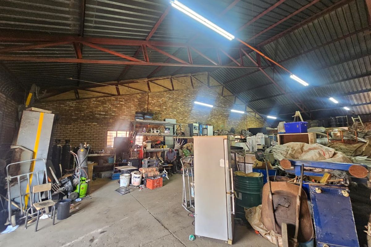 Spacious industrial utility area featuring exposed steel roof trusses, corrugated metal roofing, and durable concrete flooring with exposed brick wall finishes.