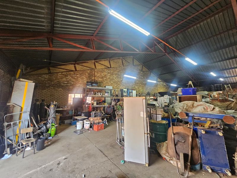 Spacious industrial utility area featuring exposed steel roof trusses, corrugated metal roofing, and durable concrete flooring with exposed brick wall finishes.